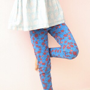 May include: A child wearing a light blue dress with a white floral pattern and blue leggings with a red and blue polka dot pattern.