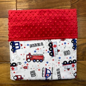May include: A red and white baby blanket with a textured red top. The bottom portion features a pattern of emergency vehicles, stars, and the words "TO THE RESCUE" and "HERO".
