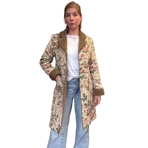 May include: A long floral coat with a cream background and a pattern of pink and green flowers. The coat has a brown faux fur collar and cuffs. The coat is open, revealing a white t-shirt and blue jeans.