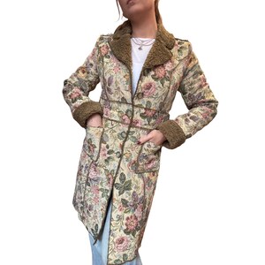 May include: A long floral coat with a cream background and a pattern of pink, purple, and green flowers. The coat has a brown faux fur collar and cuffs, with brown trim and buttons. It has two pockets.