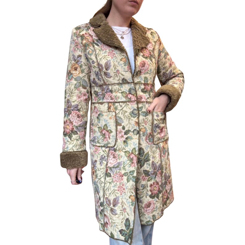 May include: A long floral coat with a cream background and a pattern of pink, purple, and yellow roses. The coat has a brown faux fur collar and cuffs, with two front pockets and a button closure. The coat is approximately 48 inches long.