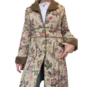May include: A long floral coat with a cream background and a pattern of pink, purple, and green flowers. The coat has a brown faux fur collar and cuffs, with matching trim and buttons. The coat has two pockets.