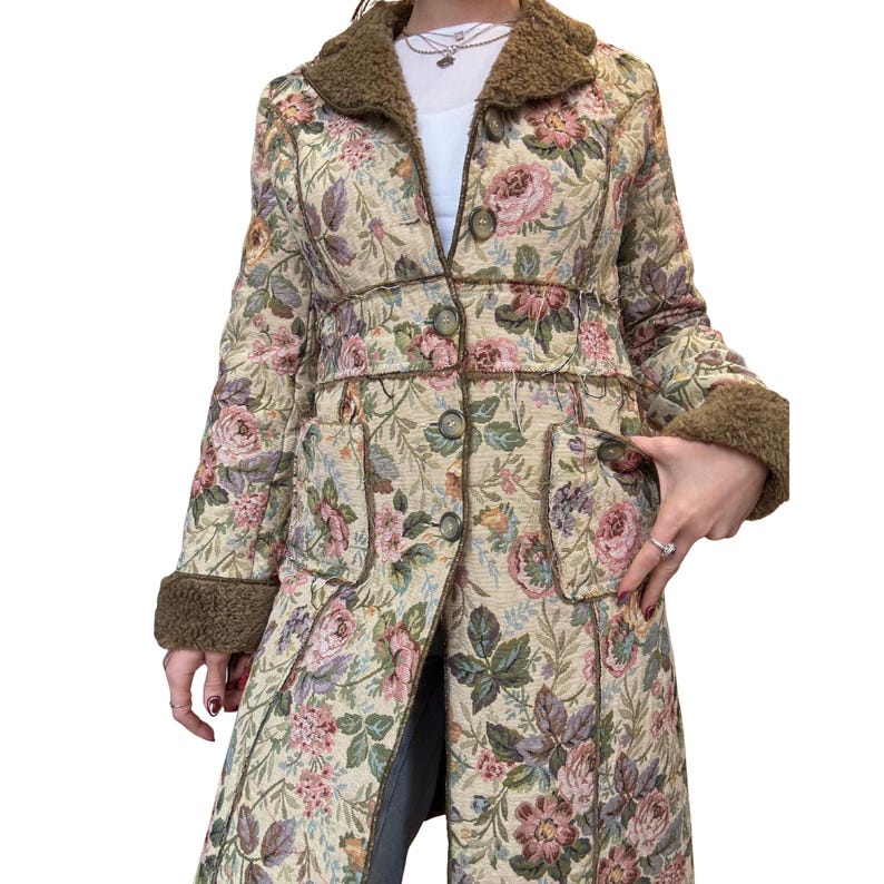 May include: A long floral coat with a cream background and a pattern of pink, purple, and green flowers. The coat has a brown faux fur collar and cuffs, with matching trim and buttons. The coat has two pockets.