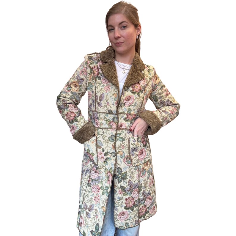 May include: A floral print coat with brown faux fur trim on the collar, cuffs, and pockets. The coat features a cream background with pink and purple roses and green leaves. The coat is knee-length and has a button closure.