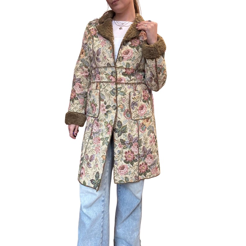 May include: A vintage floral tapestry coat with a cream background and pink, purple, and green floral pattern. The coat features brown trim, a faux fur collar and cuffs, and a button-up front. The coat measures approximately 40 inches in length.