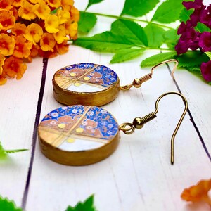 May include: A pair of gold earrings with blue and white patterned round ceramic charms. The charms have gold accents and a gold wire design.