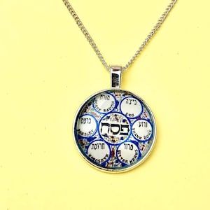 May include: Silver-toned pendant necklace with a circular charm. The charm features a colorful design with Hebrew text and English words like "Parsley" and "Egg" around the perimeter. The pendant is suspended from a delicate chain.
