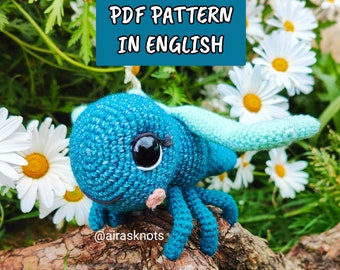 May include: A crocheted blue and green insect with large eyes and a pink nose. The insect is sitting on a branch with a white daisy in the background. The text "PDF PATTERN IN ENGLISH" is displayed above the insect. The text "@airasknots" is displayed below the insect.