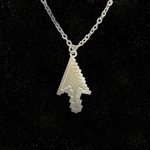 May include: A silver-colored necklace featuring a pixelated computer cursor pendant. The pendant is a stylized arrow shape, suspended from a delicate chain. The background is a solid black.