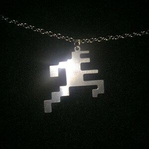 May include: A silver chain necklace with a geometric pendant in the shape of a stylized figure.