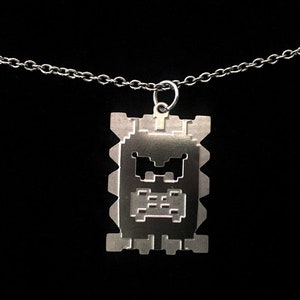 May include: A silver necklace with a pendant shaped like a pixelated face with a frowning expression.