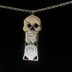 May include: A silver skull pendant necklace with a circular design on the bottom. The skull has a detailed design with crossbones and a stylized face.