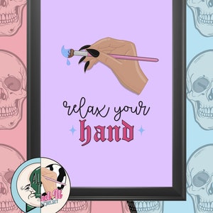 May include: Framed art print showing a hand with black nails holding a pink paintbrush with blue paint. The text "relax your hand" is in a script font. The background is a mix of pink and blue with skull illustrations.