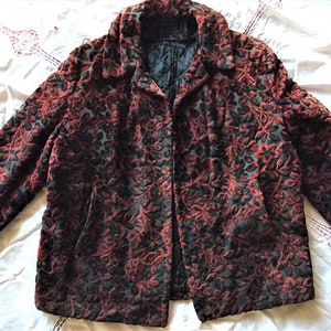 May include: A vintage jacket with a floral pattern in shades of red and black. The jacket has a classic collar and a quilted lining. The fabric has a velvet-like texture. The jacket is open in the front.