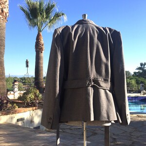 May include: A gray blazer with a belt in the back. The blazer has a slightly flared shape and is made of a textured fabric.