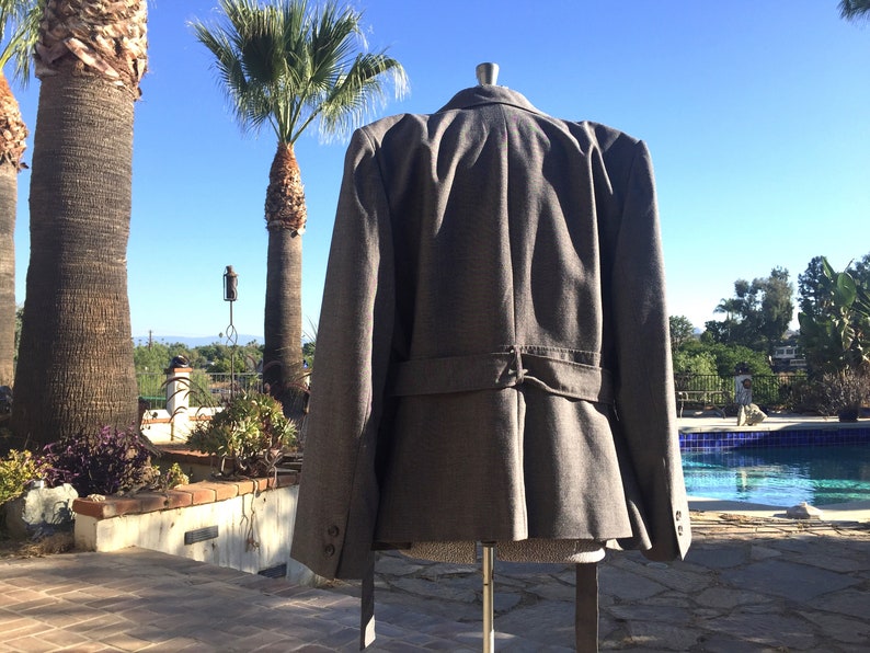 May include: A gray blazer with a belt in the back. The blazer has a slightly flared shape and is made of a textured fabric.