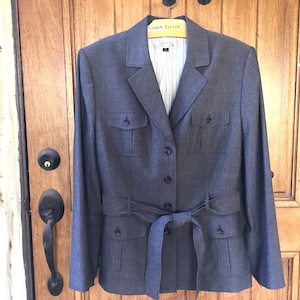 May include: A gray blazer with a belt, two flap pockets on the front, and a button closure. The blazer has a striped lining.