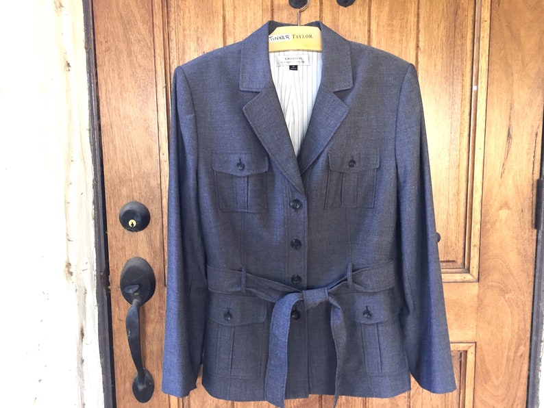 May include: A gray blazer with a belt, two flap pockets on the front, and a button closure. The blazer has a striped lining.