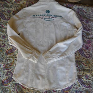 May include: A white long-sleeve button-down shirt with the text "Harley-Davidson Motorcycles" embroidered on the back.