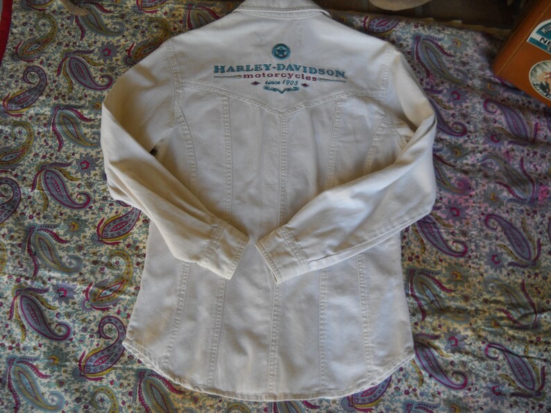May include: A white long-sleeve button-down shirt with the text "Harley-Davidson Motorcycles" embroidered on the back.