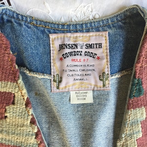 K&ouml;nnte beinhalten: Eine Jeansweste mit einem gewebten Patch, auf dem "Jensen Smith Cowboy Code Rule #7 A cowboy is kind to small children, old folks and animals." steht. Die Weste ist mit gewebten Patches in Rot-, Gr&uuml;n- und Beiget&ouml;nen verziert.