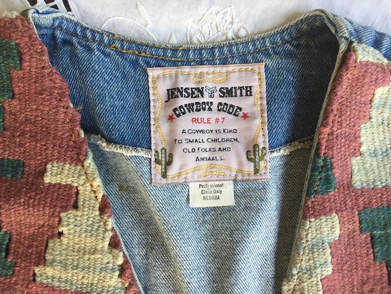 K&ouml;nnte beinhalten: Eine Jeansweste mit einem gewebten Patch, auf dem "Jensen Smith Cowboy Code Rule #7 A cowboy is kind to small children, old folks and animals." steht. Die Weste ist mit gewebten Patches in Rot-, Gr&uuml;n- und Beiget&ouml;nen verziert.