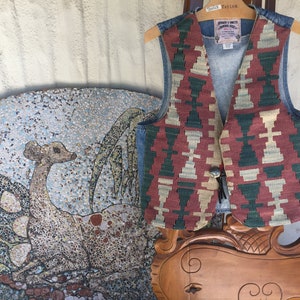 K&ouml;nnte beinhalten: Eine Jeansweste mit einem farbenfrohen geometrischen Muster auf der Vorderseite. Die Weste hat einen braunen Lederriemen und einen Metallknopfverschluss. Die Weste ist von "Jonah & Smith" hergestellt und hat ein "Vintage Style" Etikett.