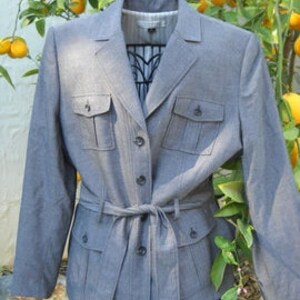 May include: A gray blazer with a belted waist and multiple pockets. The blazer has a subtle pinstripe pattern.