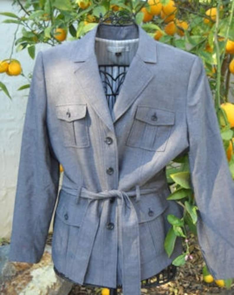 May include: A gray blazer with a belted waist and multiple pockets. The blazer has a subtle pinstripe pattern.