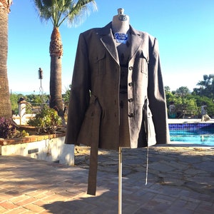 May include: A gray tweed blazer with a belt and multiple pockets. The blazer has a button closure and a collar.