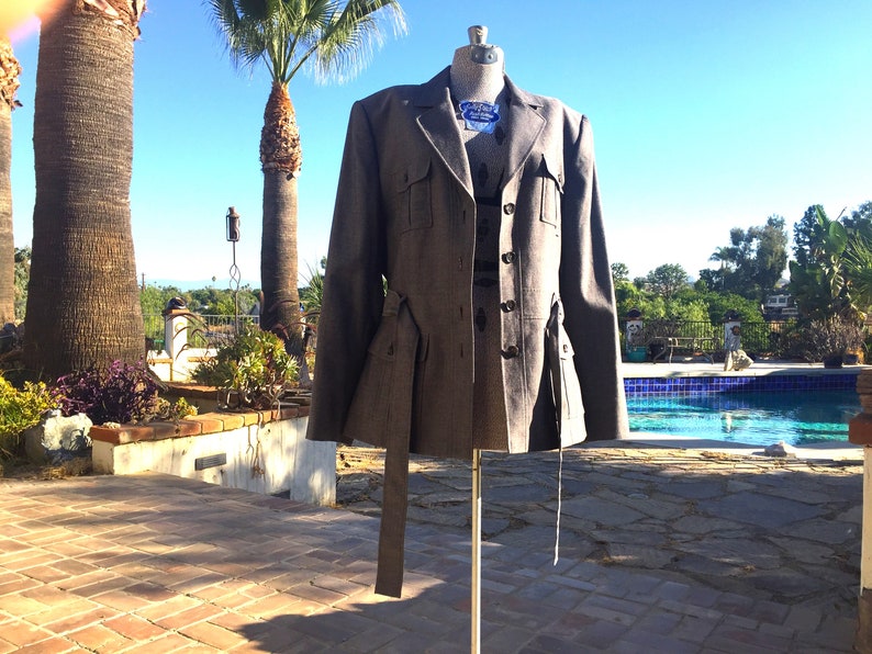 May include: A gray tweed blazer with a belt and multiple pockets. The blazer has a button closure and a collar.