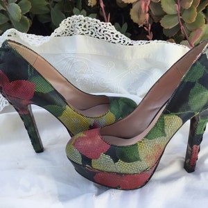 May include: A pair of platform high heels with a floral pattern in red, yellow, and green on a black background. The heels have a stiletto heel and a platform sole. The shoes are displayed on a white surface.