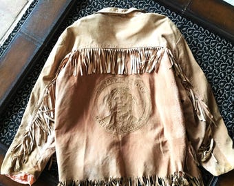 May include: A brown suede jacket with fringe detailing and a Native American-inspired design on the back. The design features a Native American man's face with the text "Native Funks" and "America's Voice".