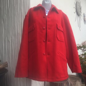 May include: A bright red wool jacket with a button-up front and two large flap pockets. The jacket has a classic workwear style.