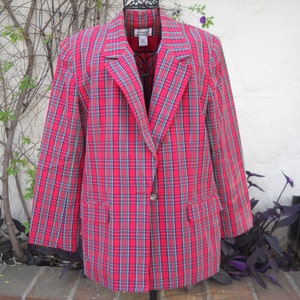 May include: A red plaid blazer with a single-button closure and two front pockets. The blazer features a classic plaid pattern in red, blue, and green. The blazer is displayed on a hanger.
