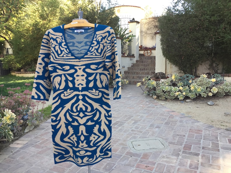 May include: A blue and beige patterned sweater dress with a v-neck and three-quarter sleeves.