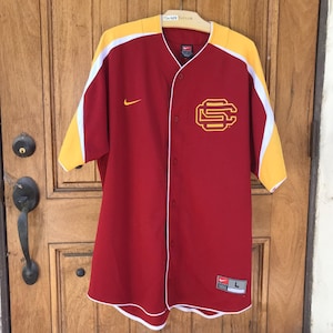 May include: A red baseball jersey with yellow and white accents. The jersey features a button-up front, short sleeves, and the Nike logo. A gold and white "SC" logo is on the chest. The jersey is size L.