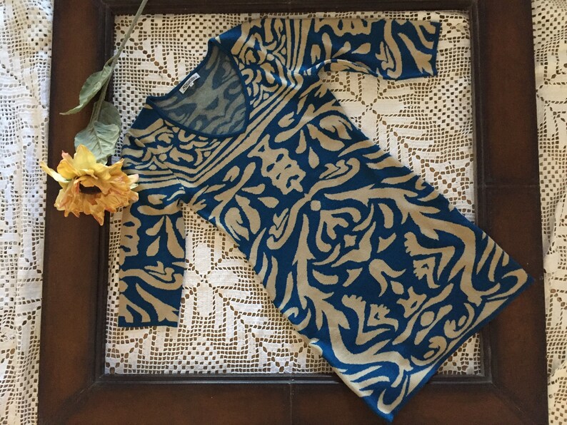 May include: A teal blue and beige patterned sweater dress with a v-neck.