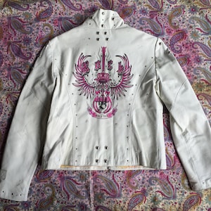 May include: White leather jacket with a pink and white graphic design of a guitar, wings, and a crown. The graphic says "Rock" and "World Tour".