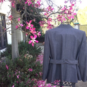 May include: A gray blazer with a belt, photographed against a backdrop of a tree with pink blossoms.