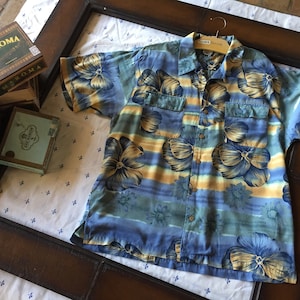 TOMMY BAHAMA HAWAIIAN Shirt in size Large features a Floral print in Blues and Golds Cotton Rayon Blend  2 front envelope pockets