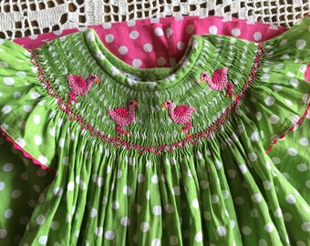 May include: Green and white polka dot dress with pink flamingo embroidery on the neckline.