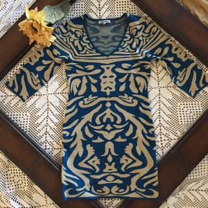 May include: A teal and beige patterned sweater dress with a V-neck and three-quarter sleeves.