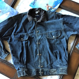 May include: A dark blue denim jacket with a brown corduroy collar. The jacket has a button closure, two flap pockets, and a ribbed waistband.