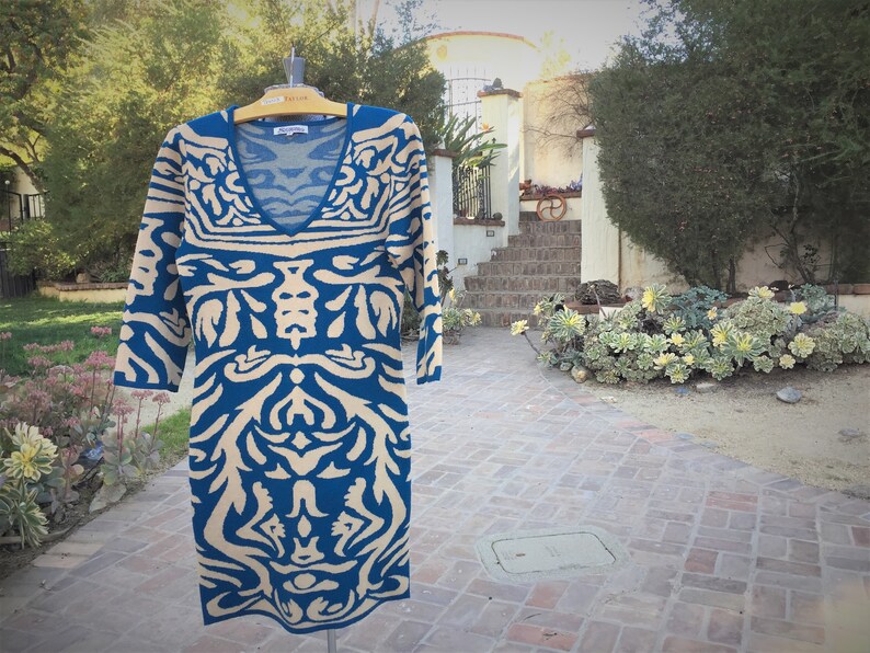 May include: A blue and beige patterned sweater dress with a v-neck. The dress is on a hanger and has a tag that says "Lauren Ralph Lauren".