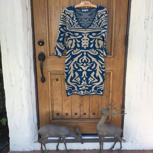 May include: A teal and beige patterned dress with a v-neck and 3/4 sleeves hanging on a hanger in front of a wooden door.