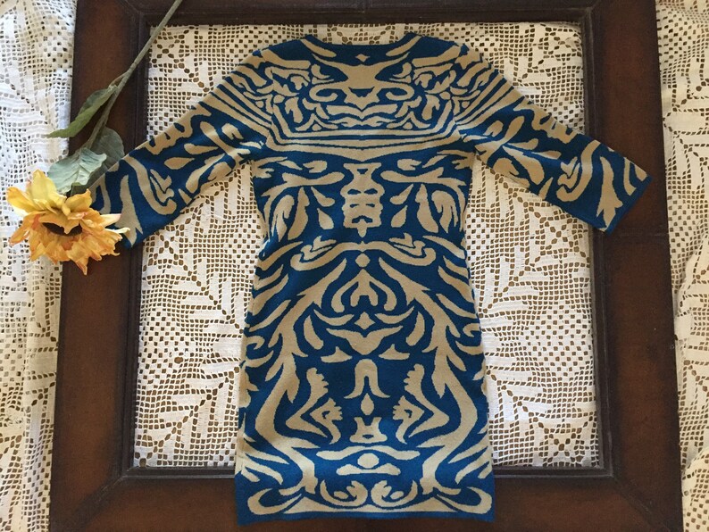 May include: A blue and beige patterned sweater dress with a long sleeve and a crew neck.