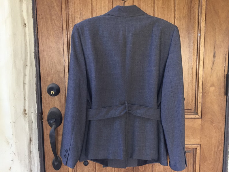 May include: A dark gray blazer with a belt in the back. The blazer has a classic style and is made of a textured fabric.