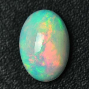 May include: An oval-shaped opal gemstone with a vibrant play of color. The opal displays a mix of green, blue, pink, and yellow hues, creating a shimmering effect. The stone is set against a dark, textured background.