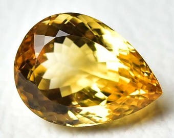 May include: A faceted, pear-shaped gemstone with a warm yellow hue, transitioning to a deeper amber at the base. The gem's cut creates multiple reflective surfaces, enhancing its brilliance. The stone is set against a white background.